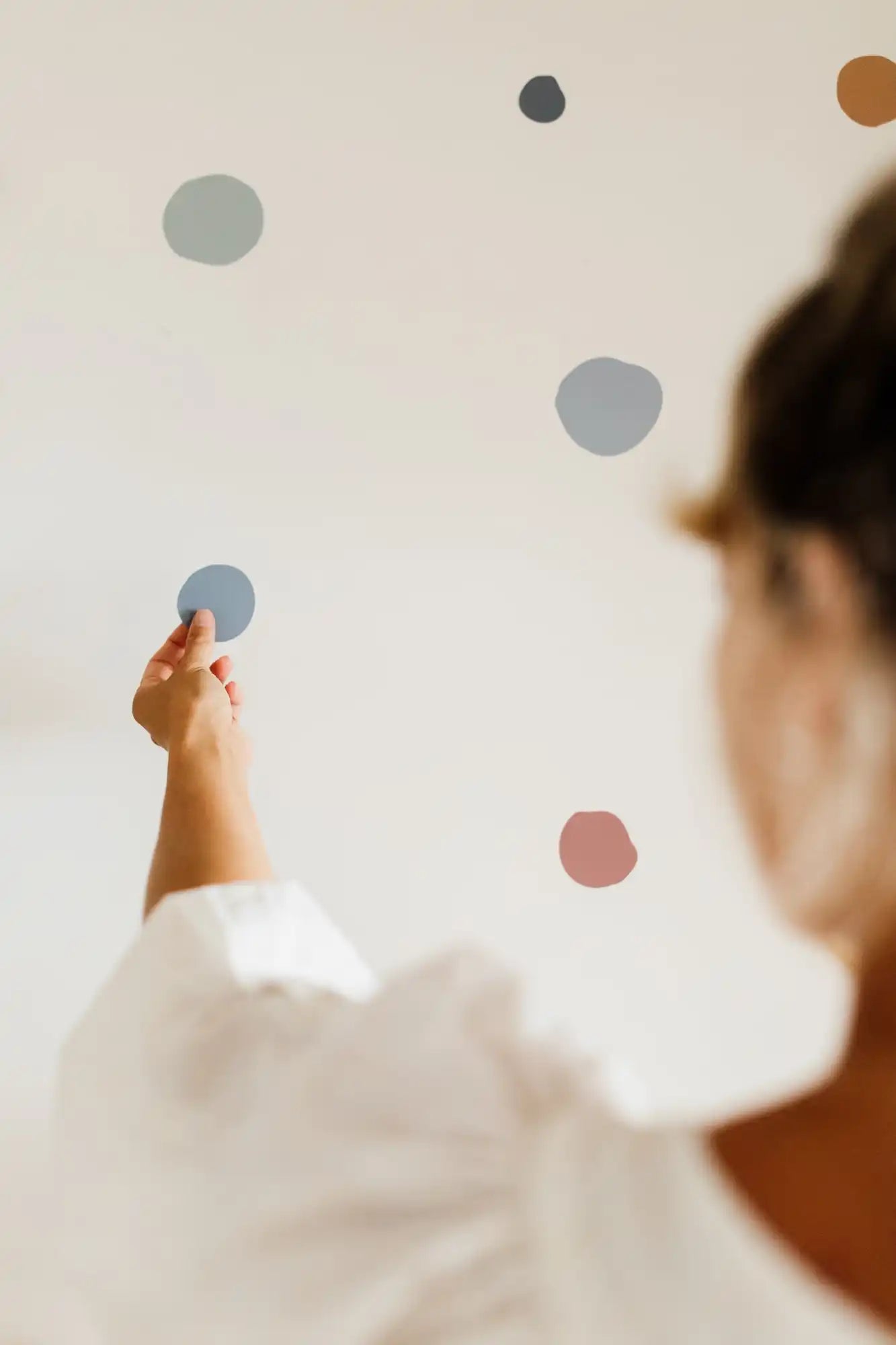 A hand pointing at colorful polka dots on a wall.